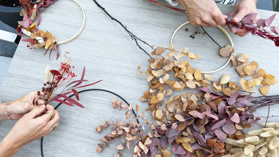 Hands crafting autumn wreaths on table.