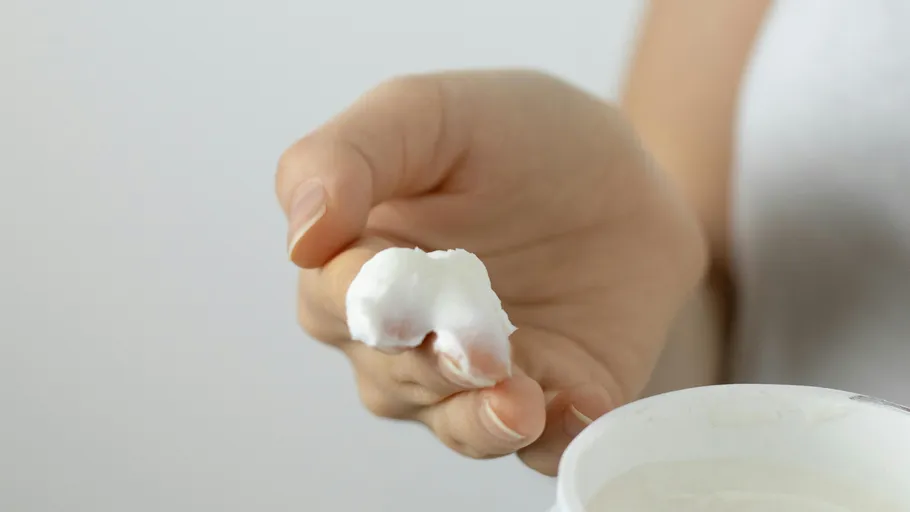 Hand hält weiße Creme, Dose im Hintergrund.
