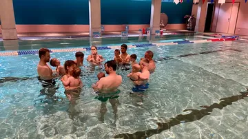 Erwachsene halten Babys im Hallenbad.