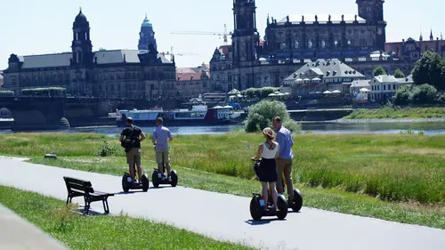People riding segways near river and historic buildings.
