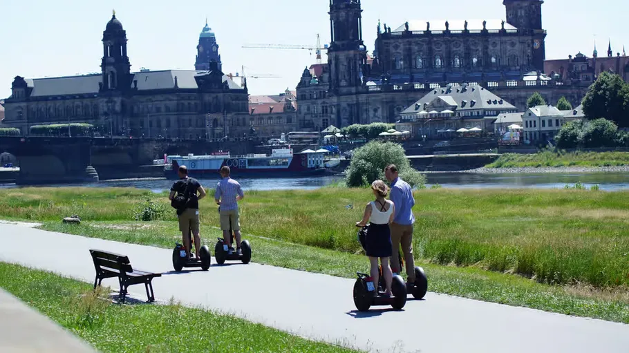 Personen fahren Segways am Fluss und historischen Gebäuden.