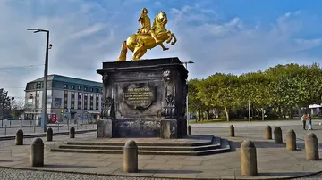 Goldene Pferdestatue auf städtischem Platz.