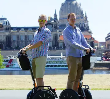 Zwei Personen auf Segways in städtischer Umgebung.