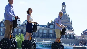 Three people ride Segways near historic buildings.