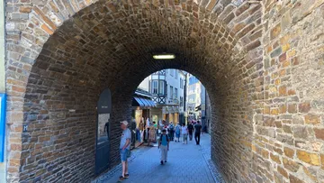 People walking through stone archway in city.