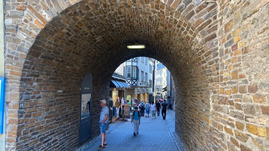 Menschen gehen durch steinernen Torbogen in Stadt.