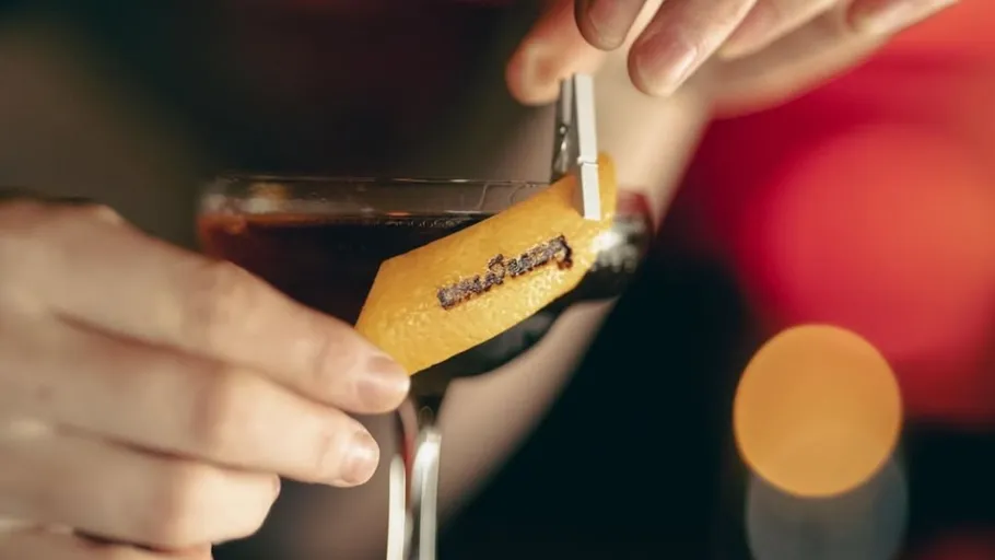 Hand placing a lemon peel on a cocktail.