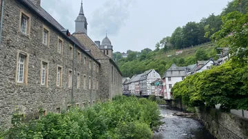 Historische Gebäude an einem fließenden Fluss im Waldgebiet.