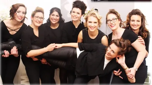 Group of women holding a man indoors smiling.