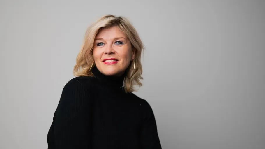 Smiling woman in black turtleneck, gray background.