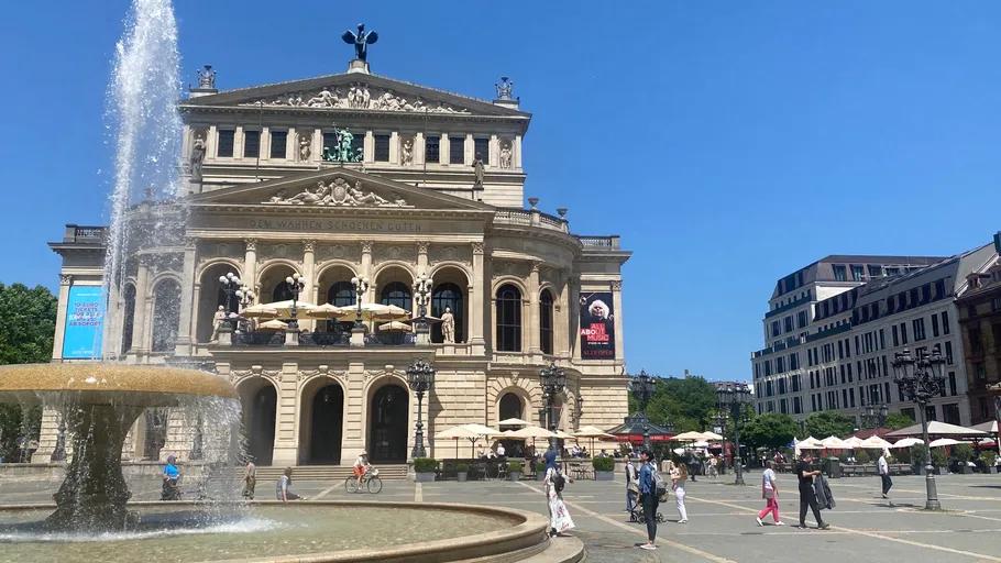 Opera house with fountain, people walking nearby.
