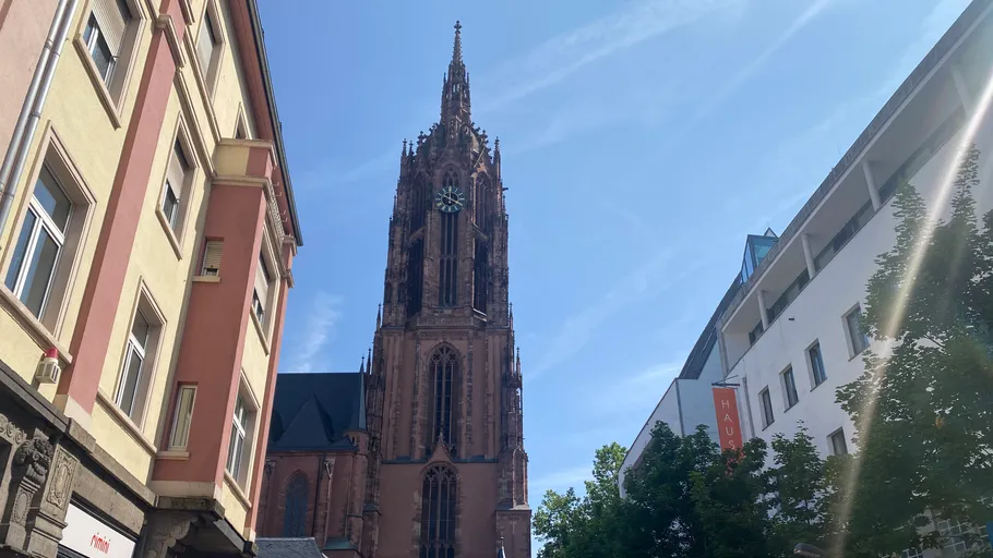 Gotischer Kirchturm zwischen städtischen Gebäuden.
