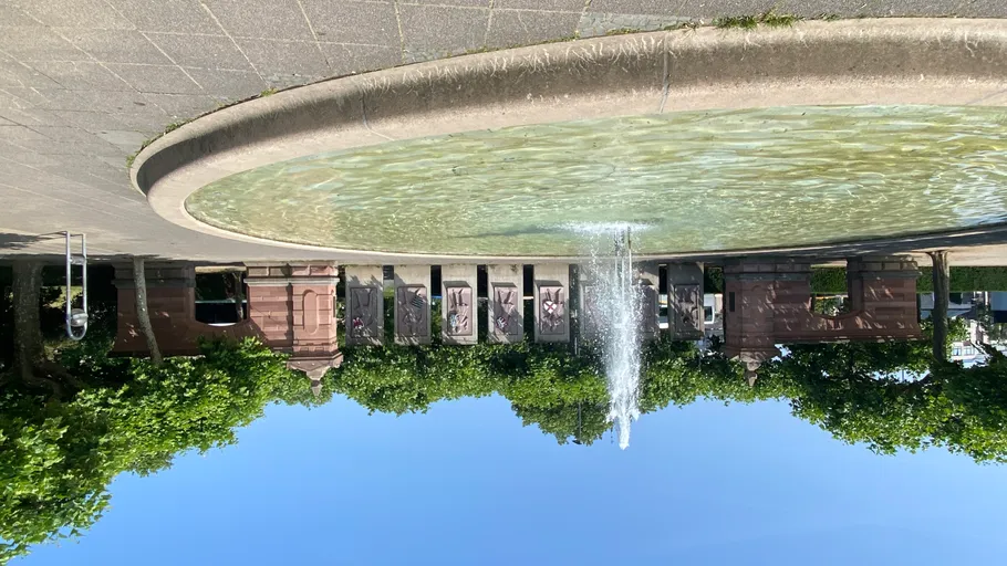 Brunnen sprüht Wasser im sonnigen Park.