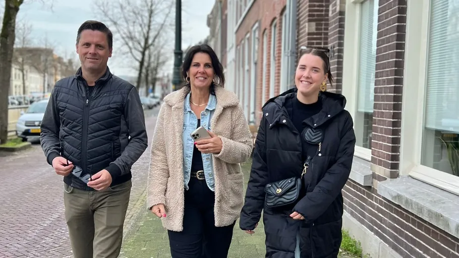 Three people walking on a sidewalk near buildings.