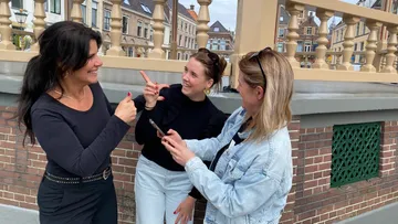 Drei Frauen lachen und benutzen ein Handy im Freien.