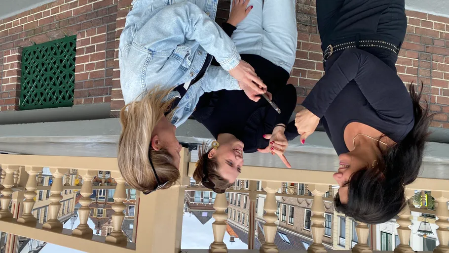 Drei Frauen lachen und benutzen ein Handy im Freien.