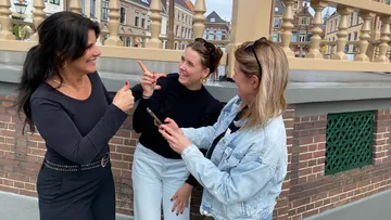 Drei Personen unterhalten sich draußen, Stadt im Hintergrund.