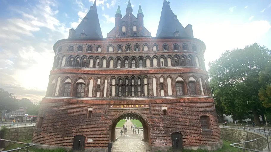 Backsteintorhaus, Fußgänger darunter, bewölkter Himmel.