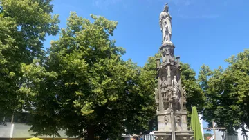 Steinstatue von grünen Bäumen umgeben.