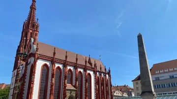 Gotische Kirche neben hohem Obelisk, Stadt im Hintergrund.