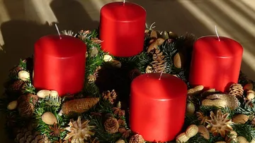Vier rote Kerzen auf einem festlichen Kranz.