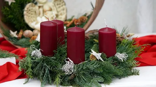 Four red candles on green wreath indoors.
