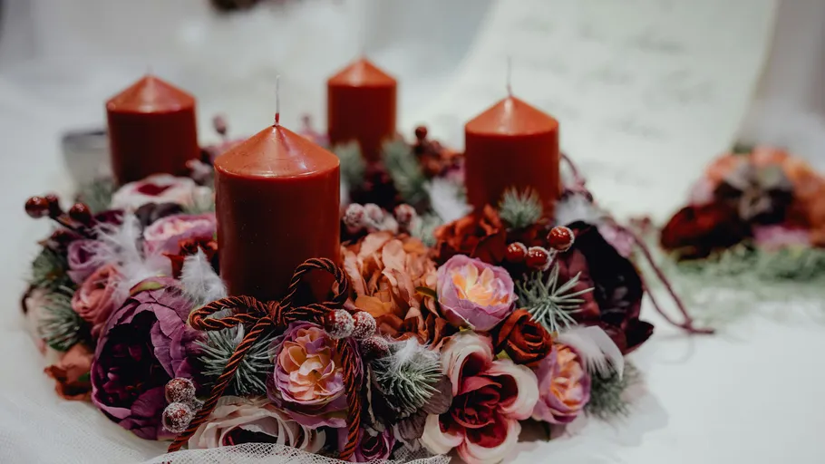 Four red candles in floral wreath indoors.