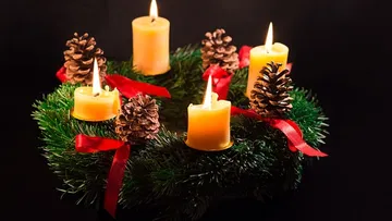 Advent wreath with four lit candles and pinecones.