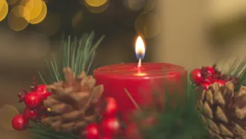 Red candle lit among pine cones.