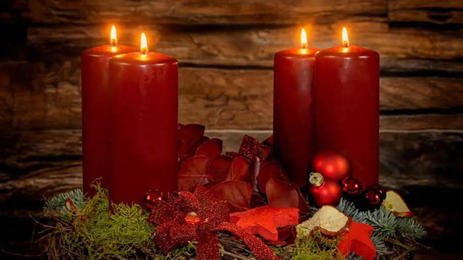 Four red candles lit on wooden background.