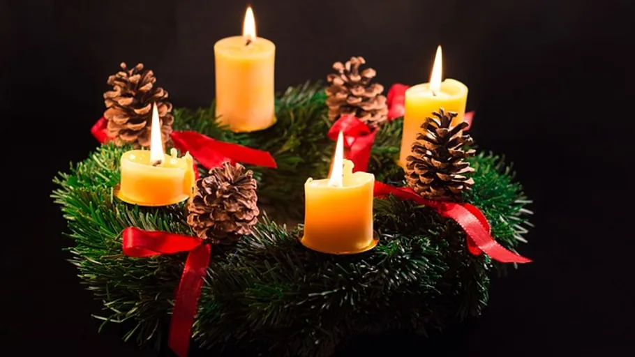 Adventskranz mit brennenden Kerzen und Tannenzapfen.