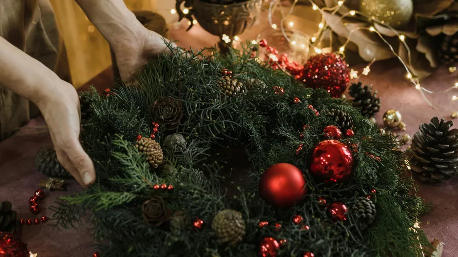 Hands arranging festive wreath with red decorations.