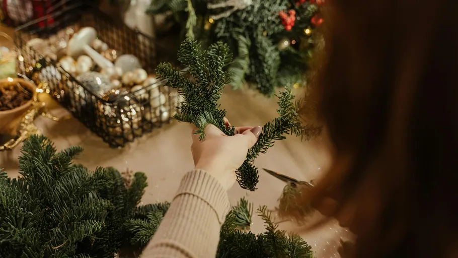 Person crafting with pine branches on table.