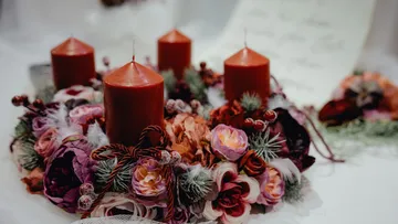 Rote Kerzen mit Blumenkranz auf Tisch.
