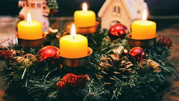 Adventskranz mit brennenden Kerzen auf Tisch.