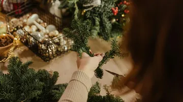 Person bastelt Weihnachtskranz mit Dekorationen.