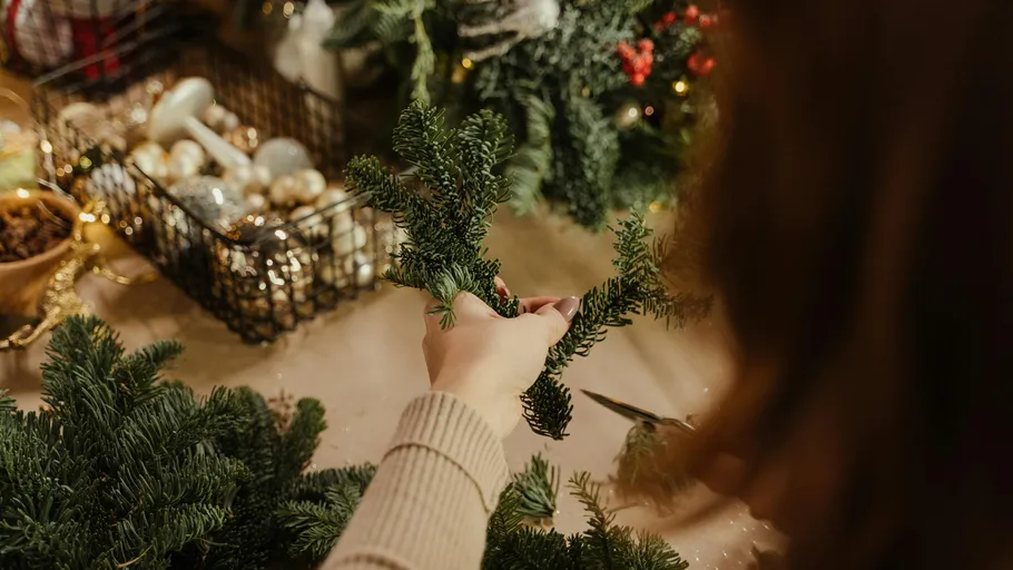 Person bastelt Weihnachtskranz mit Dekorationen.