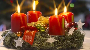 Red candles lit on Christmas wreath indoors.