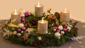 Adventskranz mit vier brennenden Kerzen und Ornamenten.