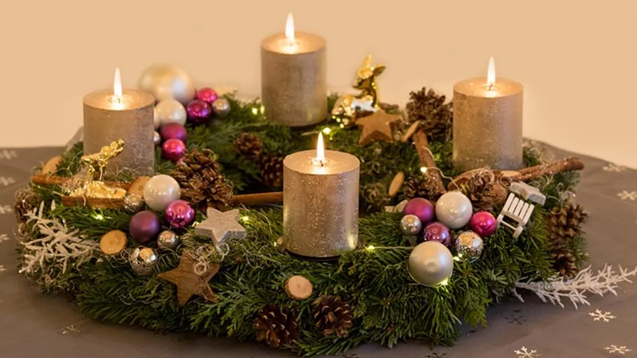 Advent wreath with four lit candles and ornaments.