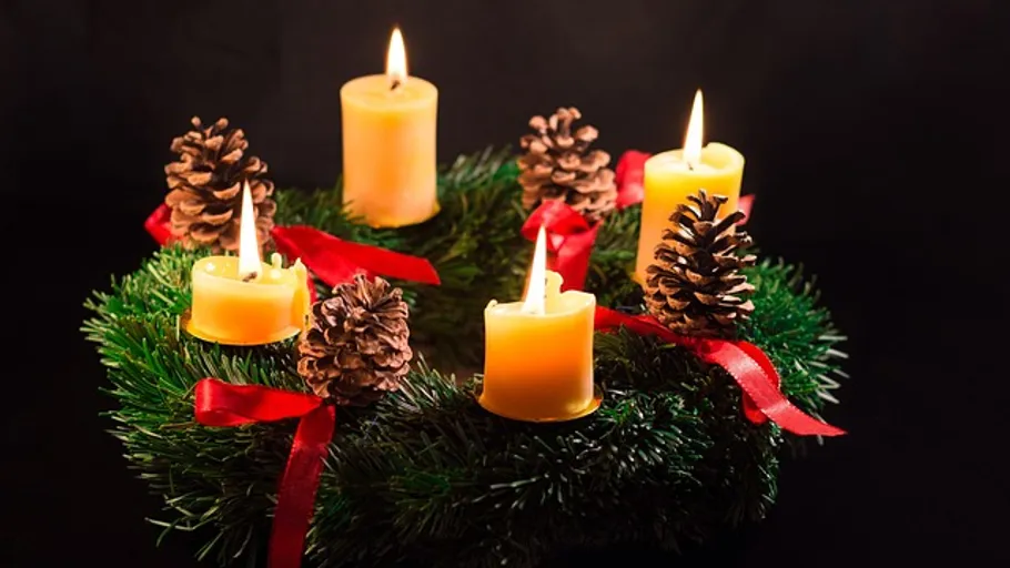 Candles and pine cones on wreath, dark background.