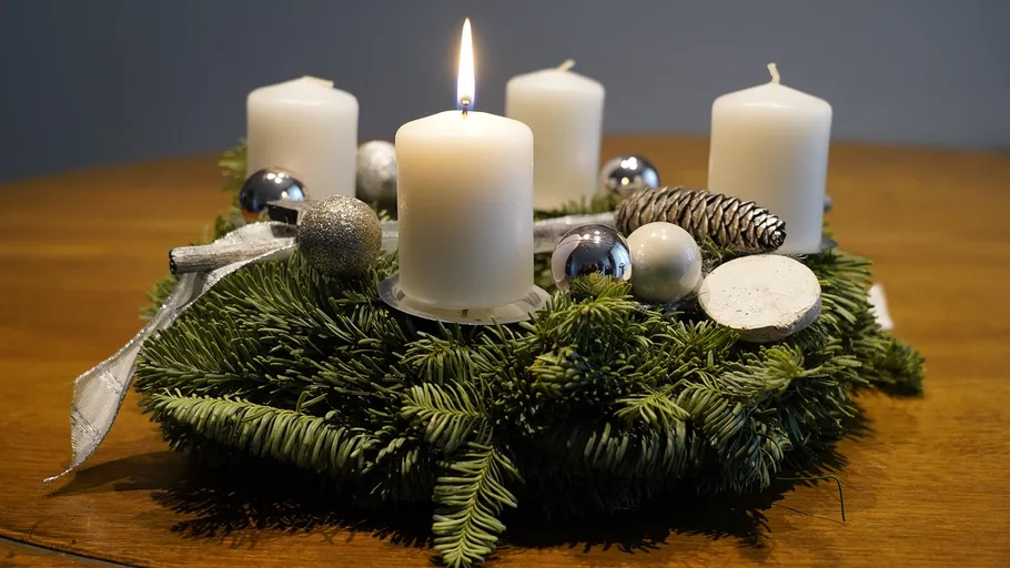 Adventskranz mit einer brennenden Kerze auf Tisch.