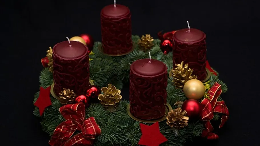 Rote Kerzen auf dekoriertem Adventskranz.