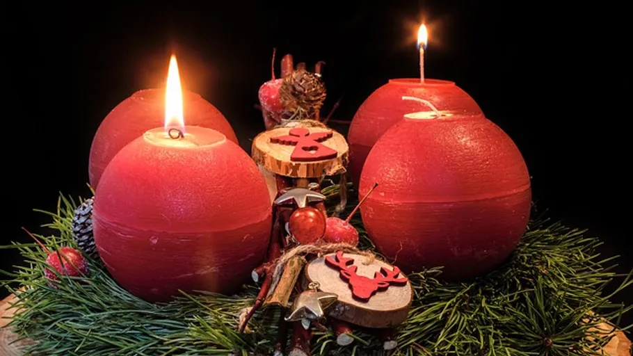 Four red candles among pine branches.