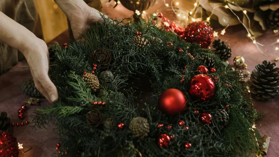 Hände arrangieren Weihnachtskranz auf Tisch.
