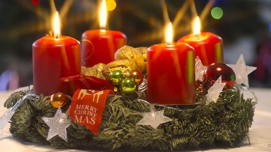 Rote Kerzen auf Adventskranz mit Dekorationen angezündet.