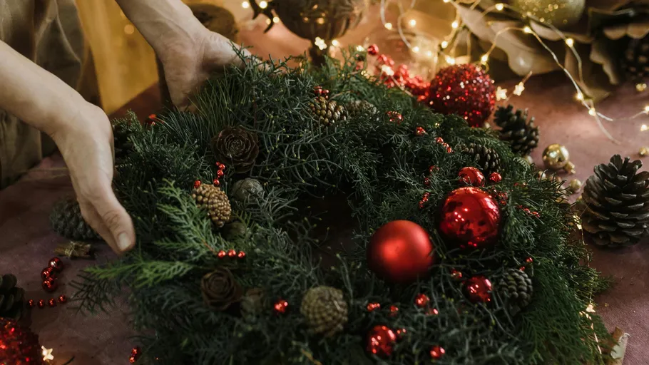 Hände dekorieren festlichen Kranz auf Tisch.