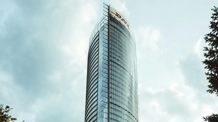 Hoher gläserner Wolkenkratzer unter bewölktem Himmel.