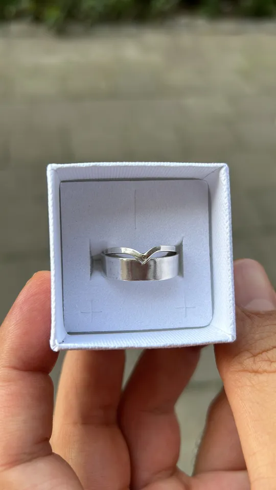 Silver ring in white box, hand holding.