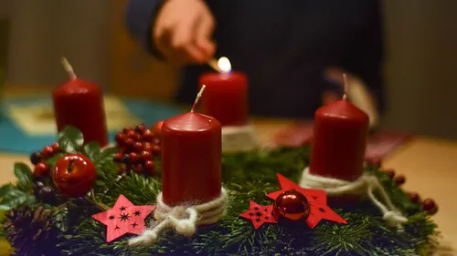 Hand zündet Kerze an festlichem Kranz an.